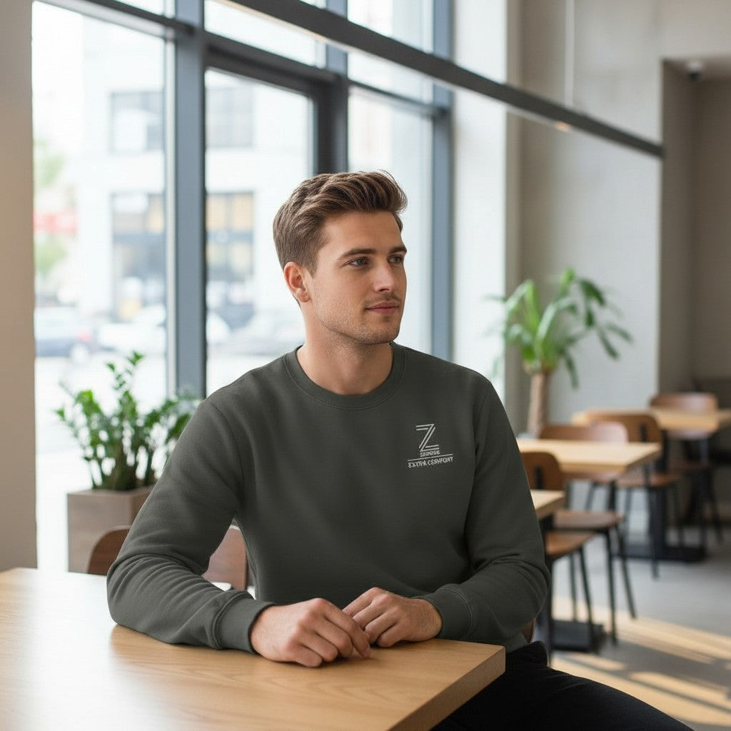 Man sitting at a table in a modern indoor setting wearing a dark gray sweatshirt with a logo.