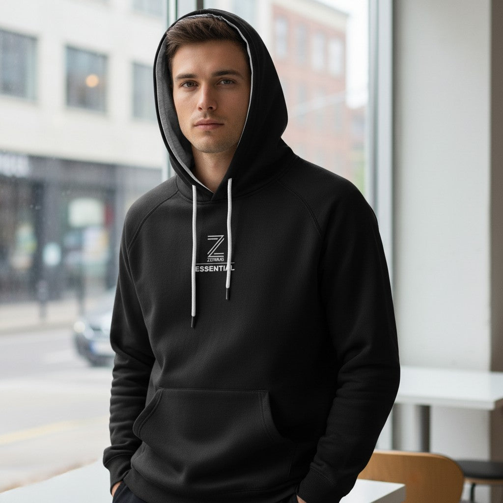 Man wearing a black hoodie with a logo, standing indoors near a window.
