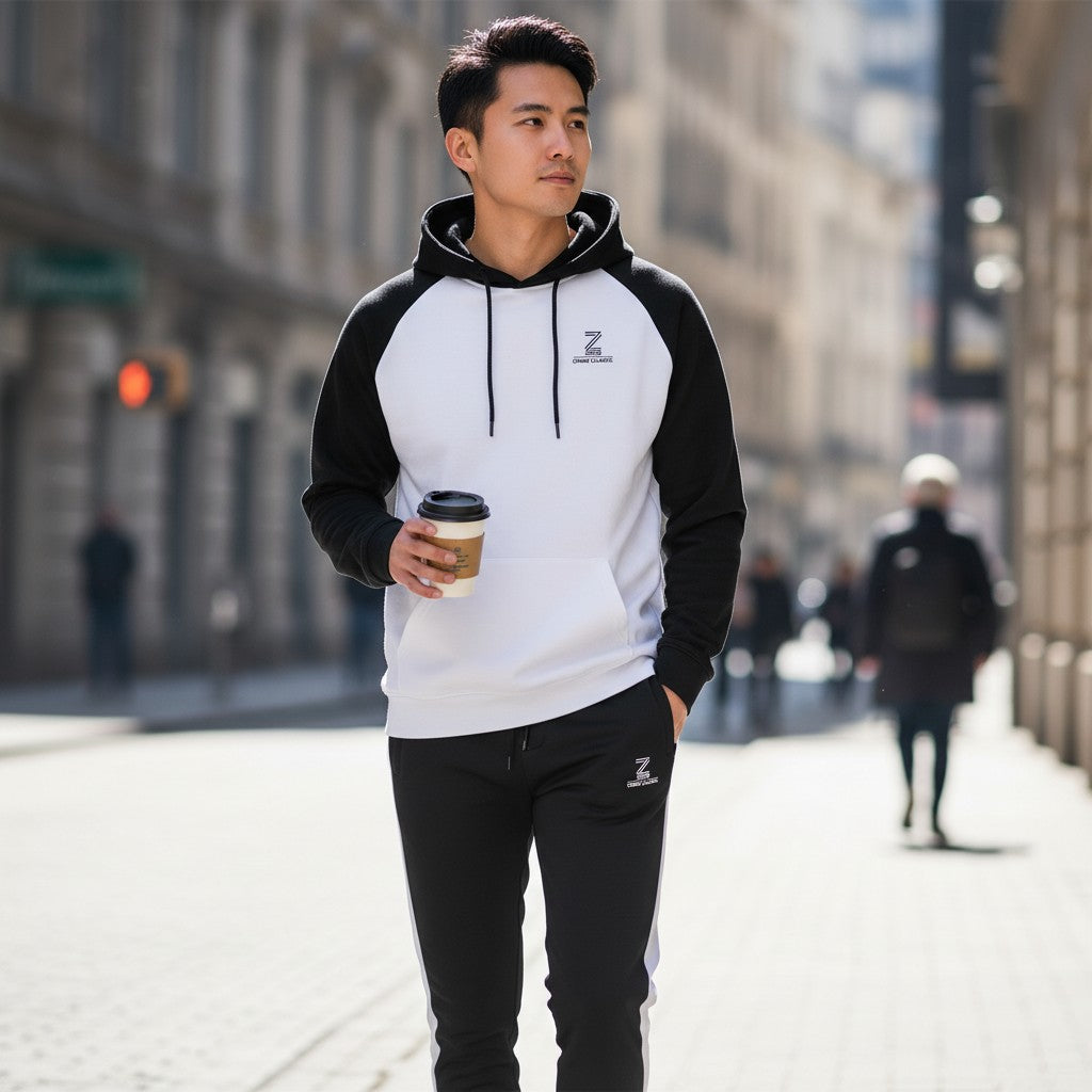 Man walking on a city street wearing a black and white hoodie with a logo, holding a coffee cup.