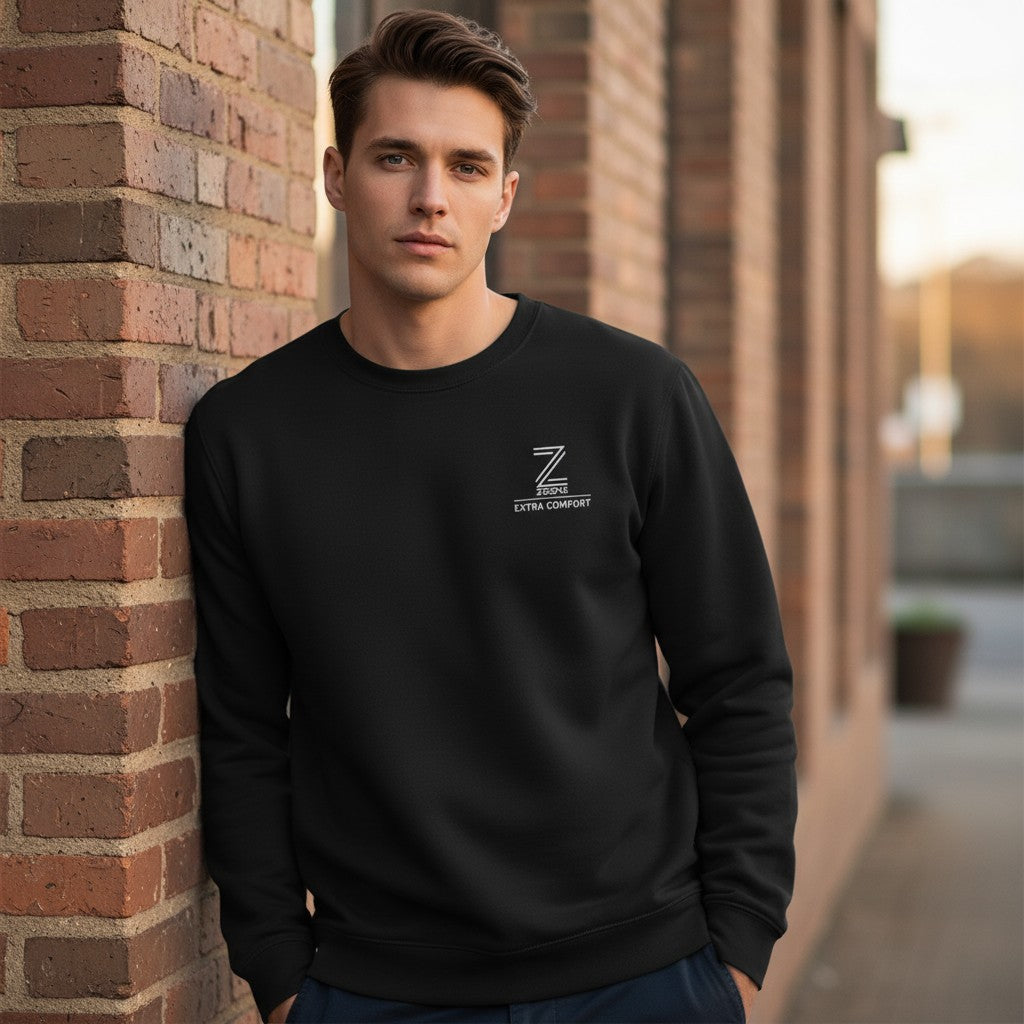 Man wearing a black sweatshirt with a logo, leaning against a brick wall.